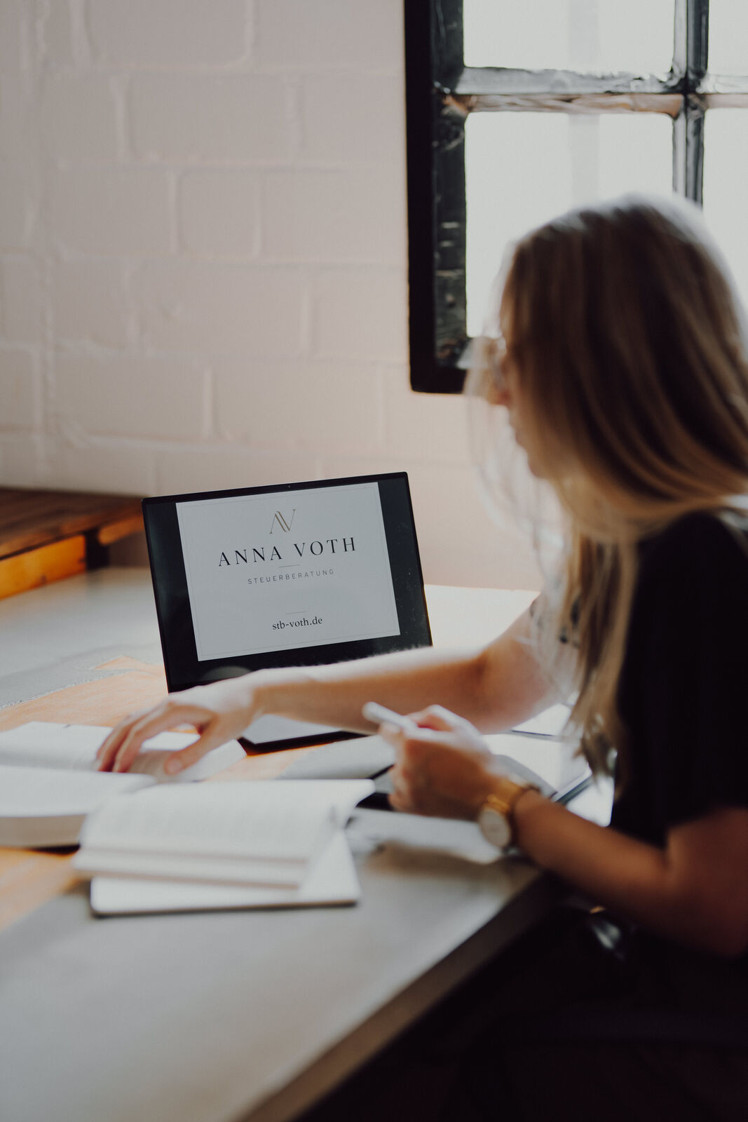 Anna Voth arbeitet am Laptop mit geöffneter Kanzlei-Startseite an einem hellen Arbeitsplatz vor einer Backsteinwand